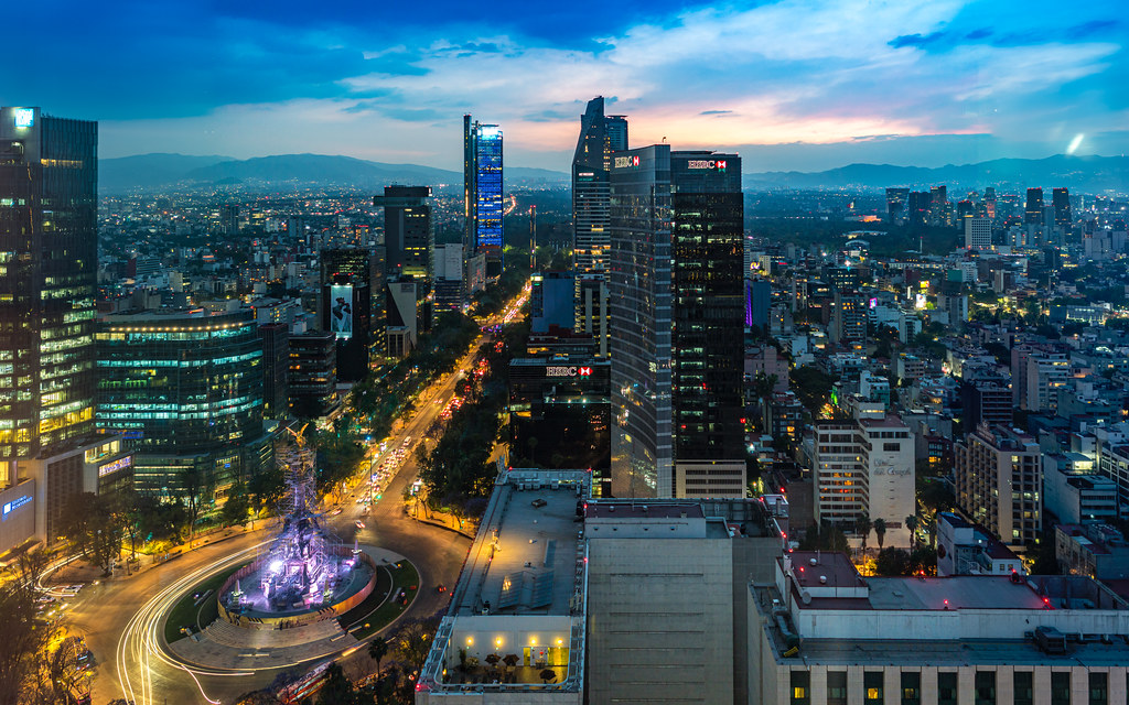 A breathtaking view of Mexico City at night, featuring the iconic Angel of Independence monument illuminated by vibrant lights, capturing the lively atmosphere and bustling nightlife of the city